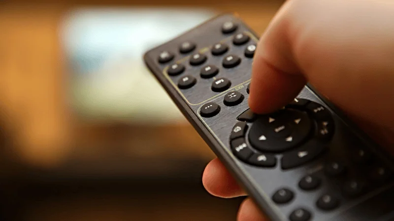 A man is pressing the membrane keyboards of the remote control.