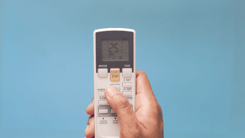 A man is pressing the membrane keyboards of the air conditioner remote control.