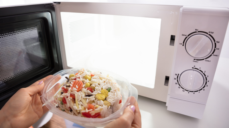 A woman is putting a silicone bowl with food into the microwave.